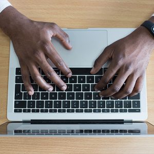 An image of a mans hands resting on laptop keys