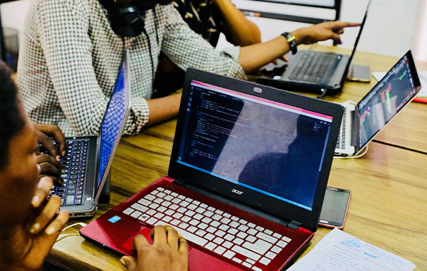 4 people work at laptops with coding script on the screen
